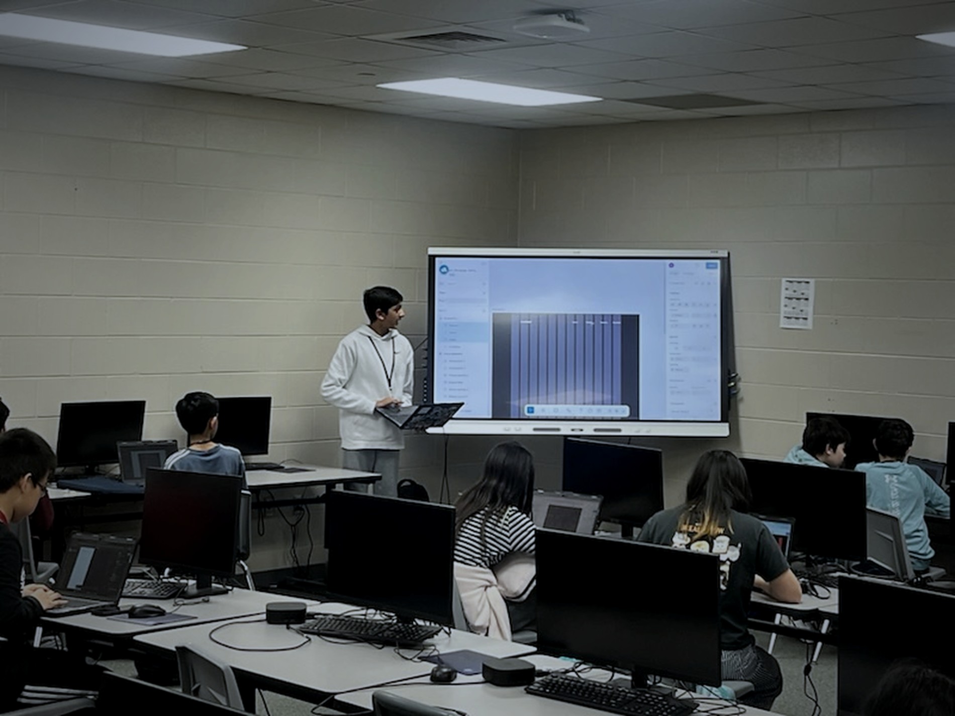 Aariv Patel teaching a design lesson at the front of a computer lab while students work at their screens